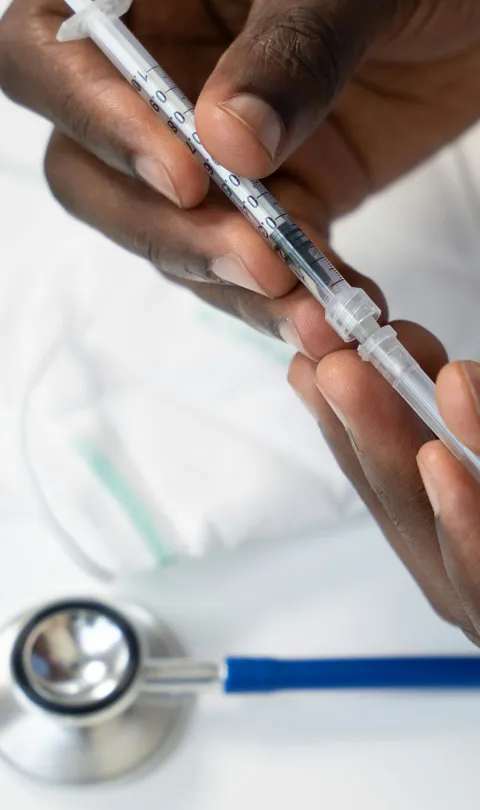 A close up of a medic's hands holding a syringe, with a stethoscope in the background. Photo by Nappy, via Unsplash