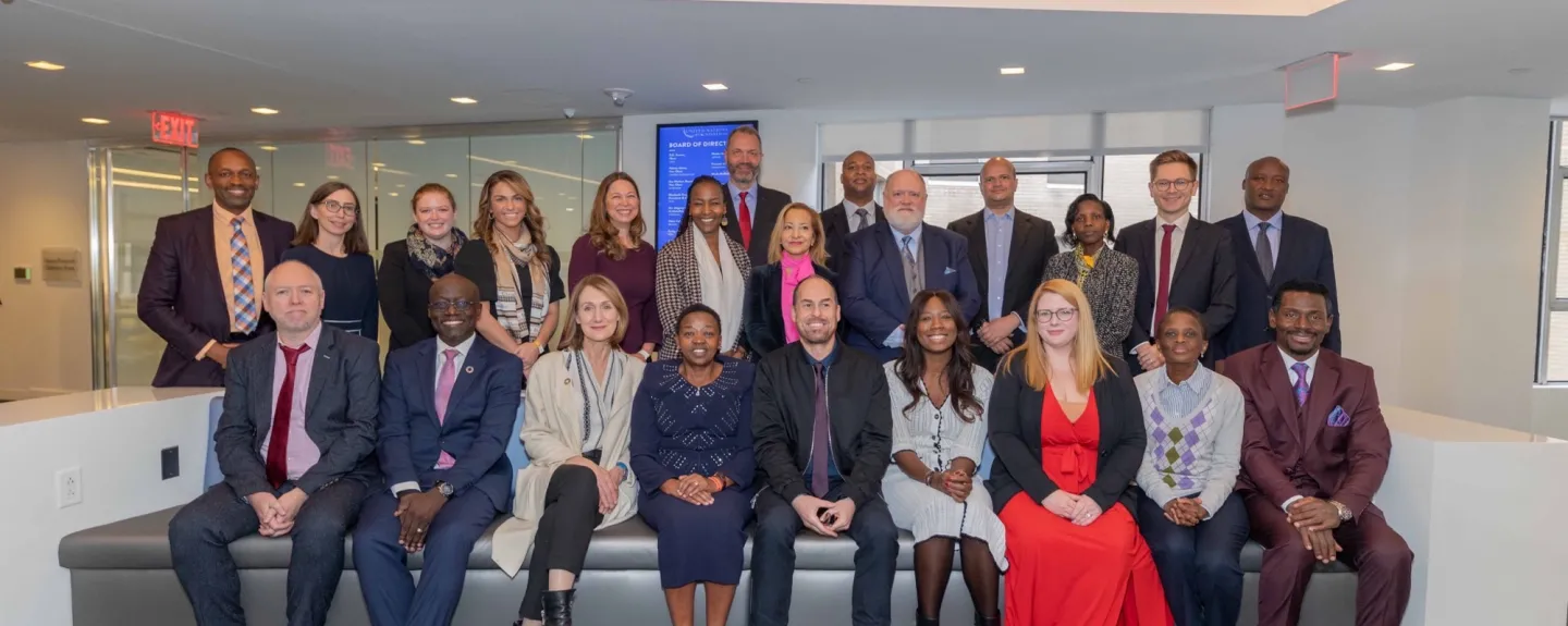 Two rows of people in a group photo. The front row is seated on a white couch. The crowd is diverse in terms of age, race, and gender, and people are wearing business clothes.